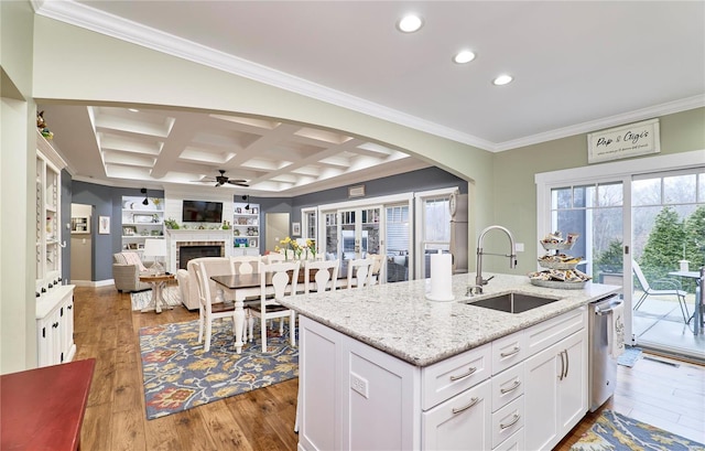 kitchen featuring sink, white cabinetry, light stone counters, coffered ceiling, and a center island with sink