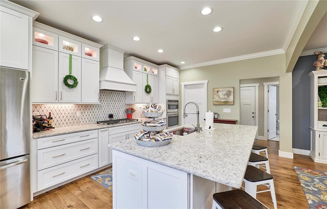 kitchen with white cabinetry, a kitchen island with sink, light stone counters, stainless steel appliances, and custom range hood