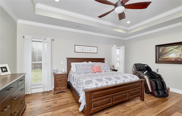 bedroom featuring multiple windows, light hardwood / wood-style floors, and a tray ceiling