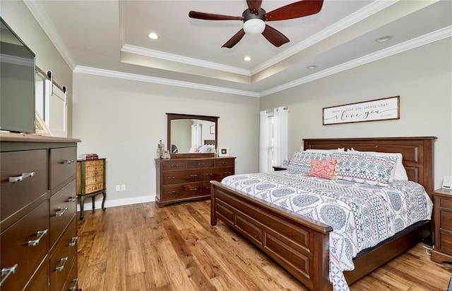 bedroom featuring light wood-type flooring, ornamental molding, a raised ceiling, ceiling fan, and a barn door