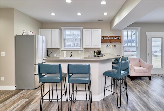 kitchen featuring white cabinetry, stainless steel fridge, a kitchen breakfast bar, hardwood / wood-style flooring, and kitchen peninsula