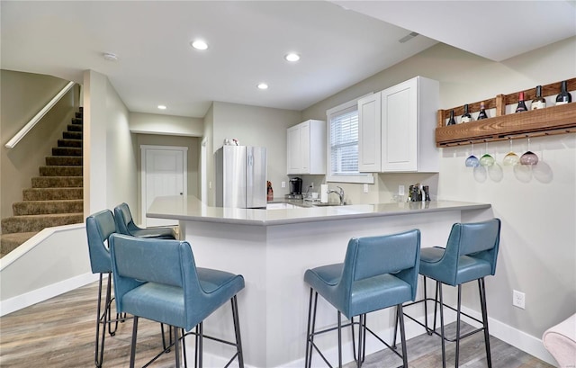 kitchen with a breakfast bar area, white cabinetry, wood-type flooring, stainless steel refrigerator, and kitchen peninsula