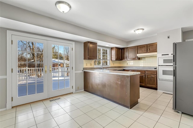 kitchen featuring white double oven, french doors, decorative backsplash, kitchen peninsula, and stainless steel refrigerator