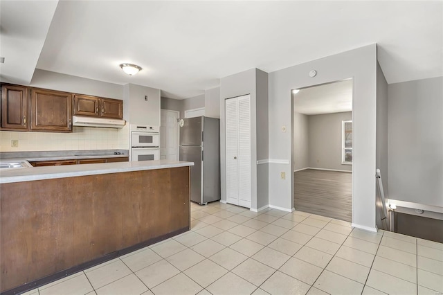 kitchen with tasteful backsplash, white double oven, light tile patterned floors, stainless steel refrigerator, and black stovetop