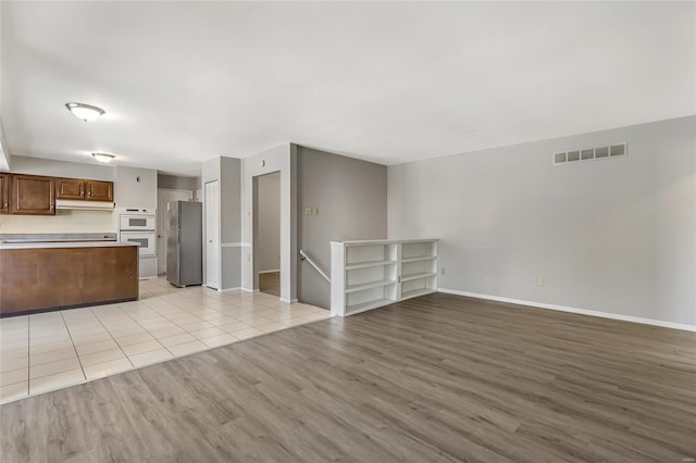 kitchen with stainless steel fridge, backsplash, and light hardwood / wood-style flooring