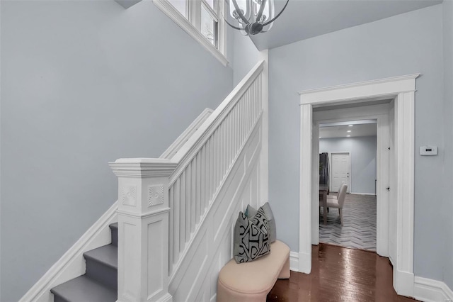 staircase with wood finished floors, a notable chandelier, and baseboards
