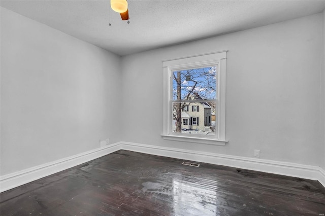 unfurnished room with dark wood-type flooring, a textured ceiling, baseboards, and visible vents