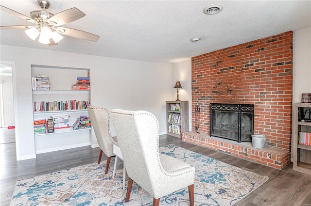 interior space with visible vents, baseboards, wood finished floors, a textured ceiling, and a brick fireplace