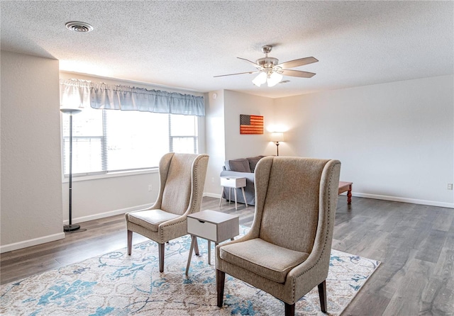 living area featuring baseboards, visible vents, a ceiling fan, wood finished floors, and a textured ceiling