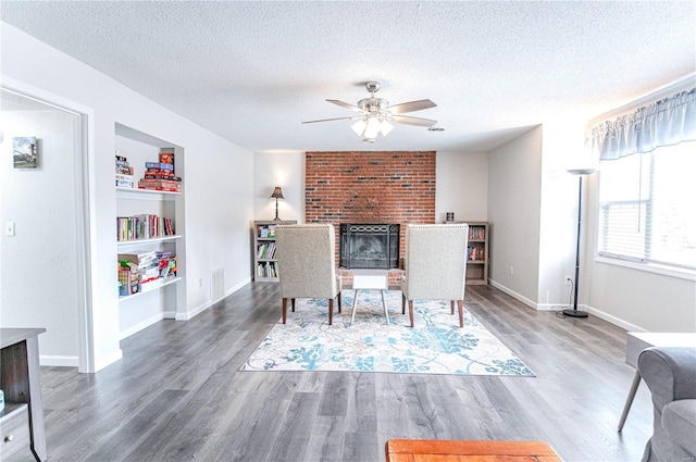 dining area with visible vents, a ceiling fan, wood finished floors, a textured ceiling, and a brick fireplace