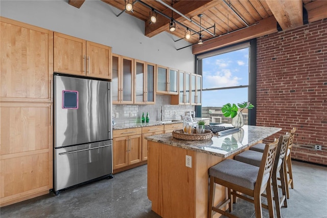 kitchen with beamed ceiling, a center island, brick wall, and stainless steel refrigerator