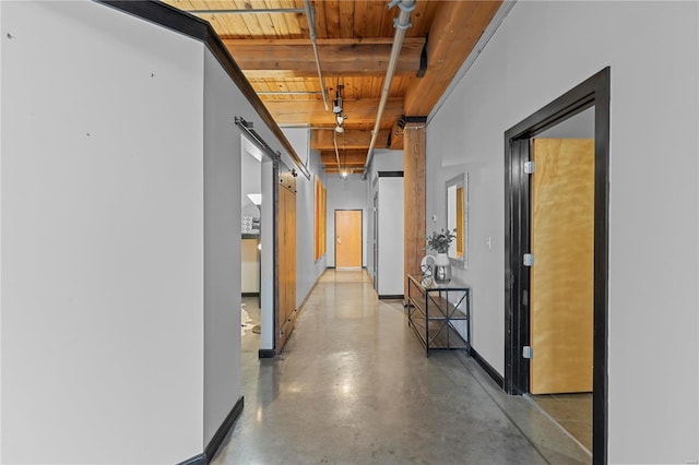 hallway with concrete flooring, beam ceiling, a barn door, and wooden ceiling