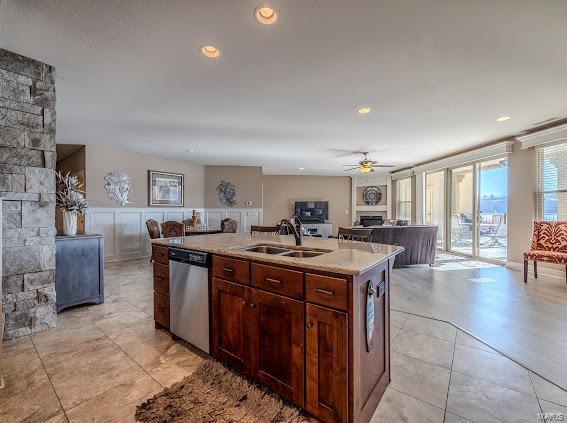 kitchen with ceiling fan, a large fireplace, sink, stainless steel dishwasher, and a kitchen island with sink