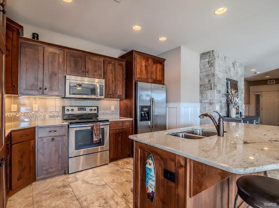 kitchen with a kitchen bar, a center island with sink, sink, light stone counters, and stainless steel appliances