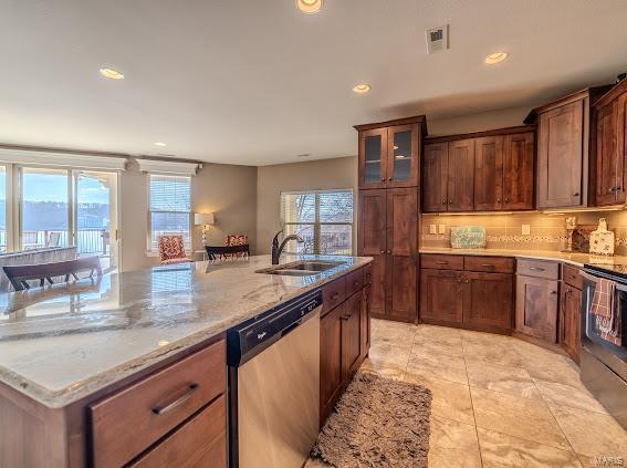 kitchen with appliances with stainless steel finishes, light stone counters, sink, light tile patterned floors, and an island with sink