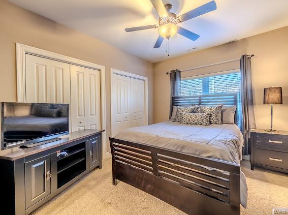 bedroom featuring light carpet, ceiling fan, and multiple closets