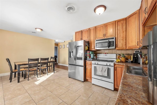 kitchen featuring sink, backsplash, light tile patterned flooring, and stainless steel appliances