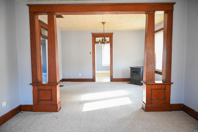 carpeted empty room with a wood stove and an inviting chandelier