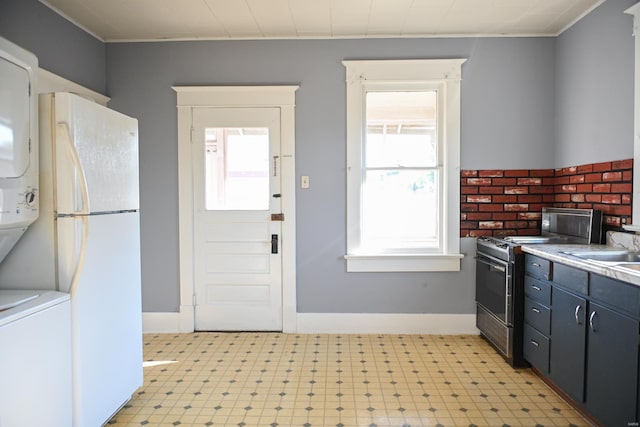 kitchen with white refrigerator, black electric range oven, plenty of natural light, and stacked washer and clothes dryer