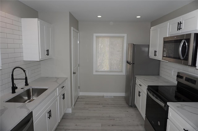 kitchen featuring sink, stainless steel appliances, light stone counters, decorative backsplash, and white cabinets