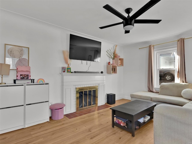 living room with a tile fireplace, ceiling fan, and light hardwood / wood-style flooring