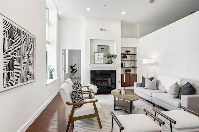 living room with dark hardwood / wood-style floors, built in features, a high ceiling, and a tile fireplace