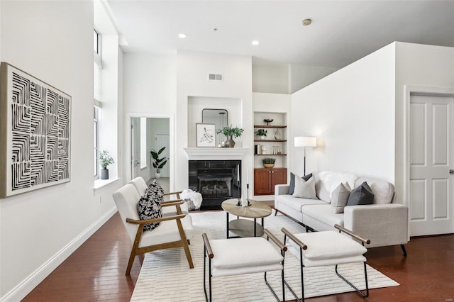 living room with dark hardwood / wood-style flooring, built in features, and a tiled fireplace