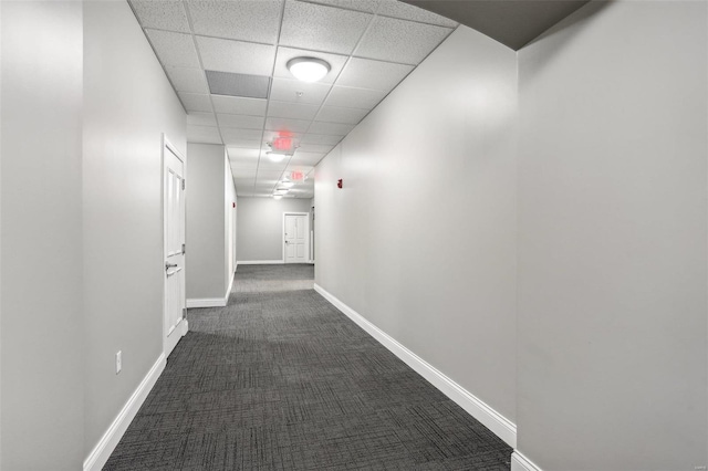 hallway featuring a paneled ceiling and dark carpet