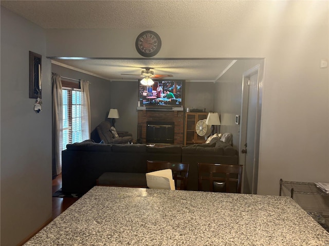 living room with ceiling fan, a fireplace, crown molding, and a textured ceiling