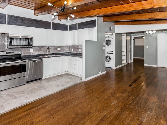 kitchen featuring backsplash, stainless steel appliances, sink, stacked washer / dryer, and beamed ceiling