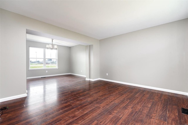 empty room featuring dark wood-type flooring and an inviting chandelier