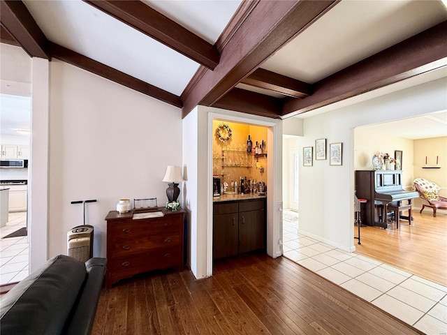 bar with dark brown cabinetry, beam ceiling, and light hardwood / wood-style floors