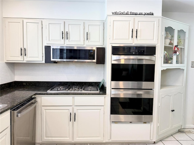 kitchen with light tile patterned floors, appliances with stainless steel finishes, white cabinets, decorative backsplash, and dark stone counters