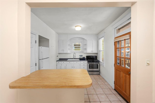 kitchen featuring white refrigerator, stainless steel range with gas cooktop, sink, light tile patterned flooring, and white cabinetry