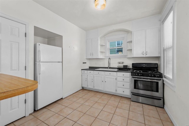 kitchen with sink, light tile patterned floors, white fridge, white cabinetry, and stainless steel range with gas stovetop