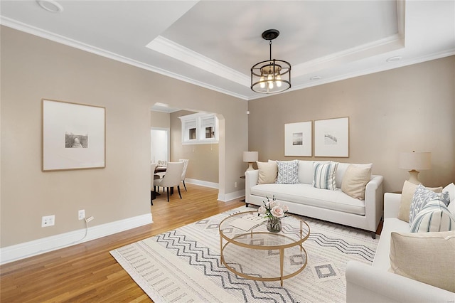 living room featuring a chandelier, wood-type flooring, a raised ceiling, and ornamental molding