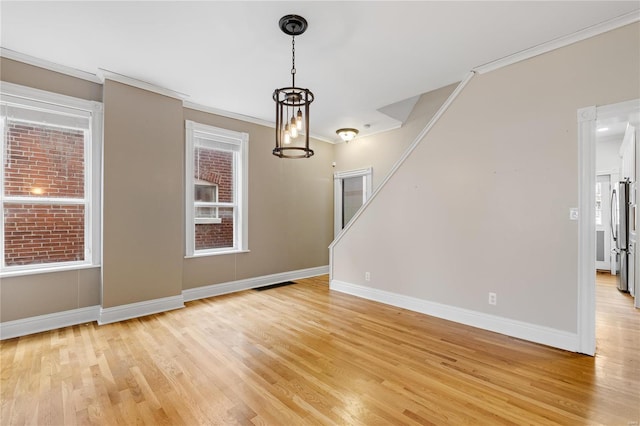 empty room with light hardwood / wood-style flooring, a wealth of natural light, ornamental molding, and a notable chandelier