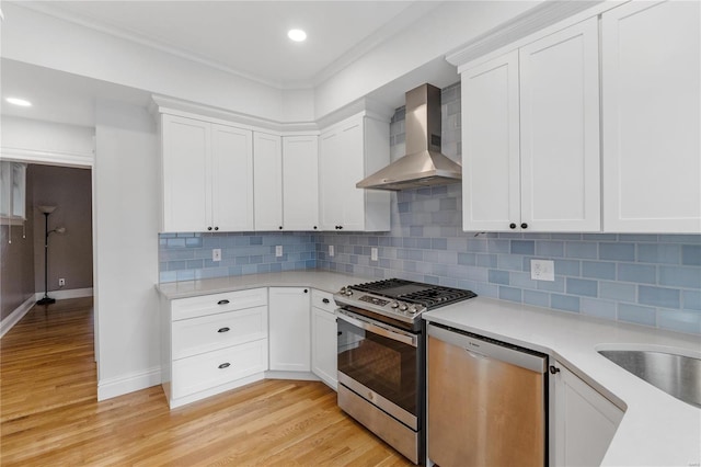 kitchen with appliances with stainless steel finishes, tasteful backsplash, wall chimney exhaust hood, white cabinets, and light hardwood / wood-style floors