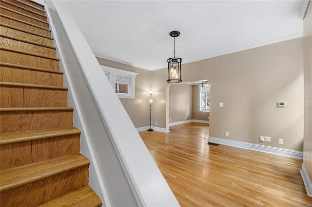 stairs with wood-type flooring, ornamental molding, and a chandelier