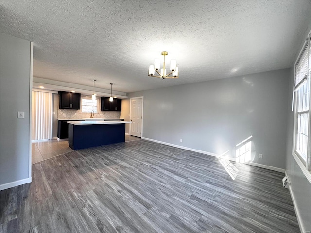 kitchen featuring dark hardwood / wood-style flooring, tasteful backsplash, an inviting chandelier, a center island, and hanging light fixtures