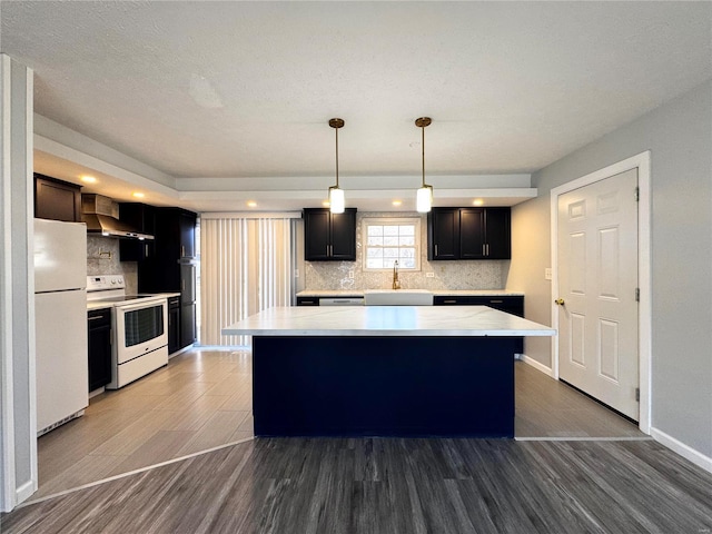 kitchen with white appliances, wall chimney range hood, decorative light fixtures, hardwood / wood-style flooring, and a center island