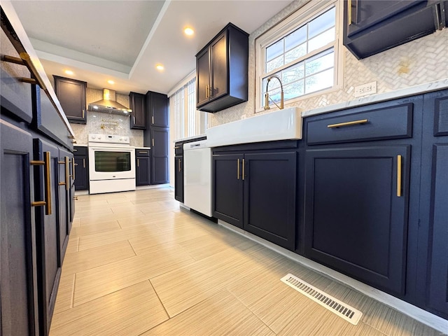 kitchen with decorative backsplash, white appliances, a tray ceiling, wall chimney range hood, and blue cabinetry