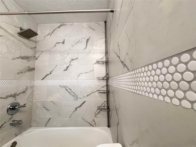 bathroom featuring a textured ceiling and tiled shower / bath