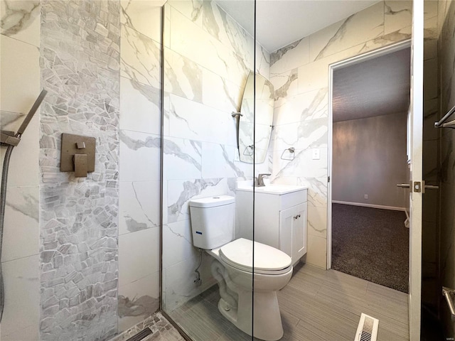 bathroom featuring tiled shower, vanity, toilet, and tile walls