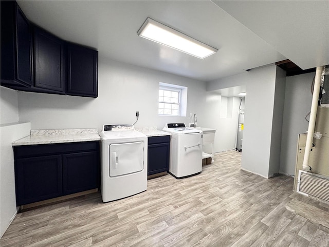 clothes washing area featuring water heater, cabinets, light wood-type flooring, and washing machine and clothes dryer