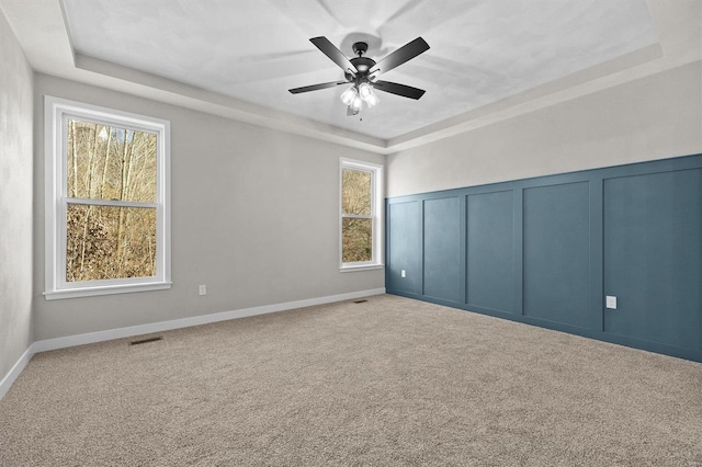 carpeted spare room with a raised ceiling and ceiling fan