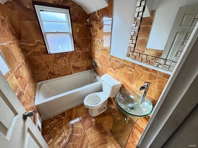 bathroom featuring tiled shower / bath combo, toilet, and tile walls