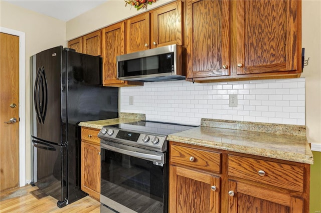 kitchen with appliances with stainless steel finishes, tasteful backsplash, light stone counters, and light hardwood / wood-style floors