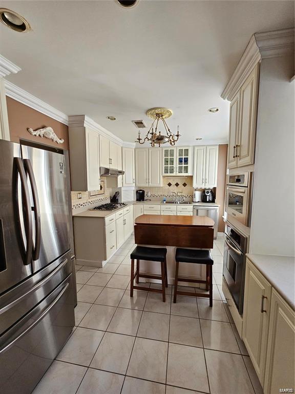 kitchen with cream cabinetry, appliances with stainless steel finishes, a kitchen breakfast bar, and light tile patterned flooring