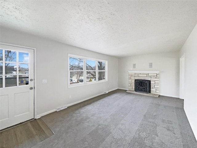 unfurnished living room featuring a stone fireplace, plenty of natural light, and a textured ceiling